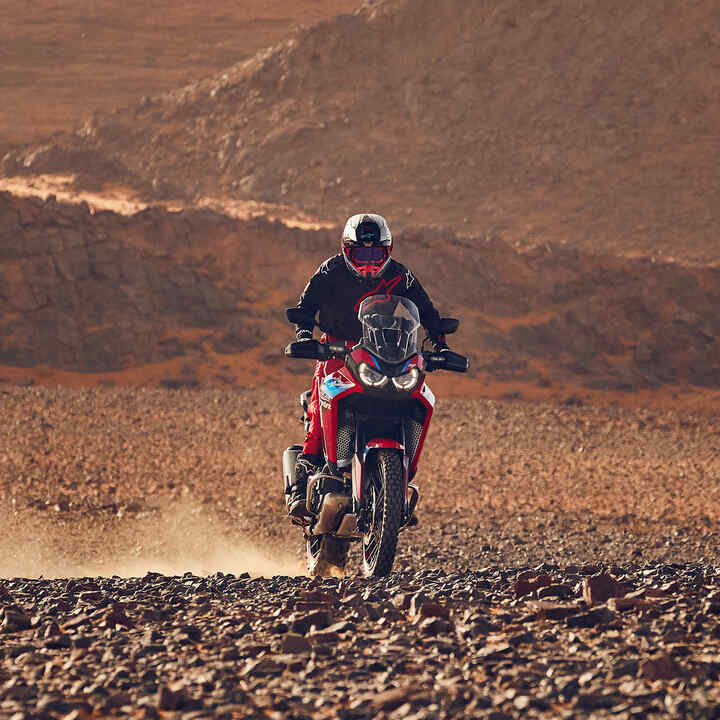Modelo conduciendo una moto CRF1100L Africa Twin en lugar desértico.